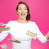 Mulher super animada, rindo, com notas de dólar voando no ar, em um fundo magenta isolado. Conceito de emoção positiva, de expressão facial e de sentimentos.