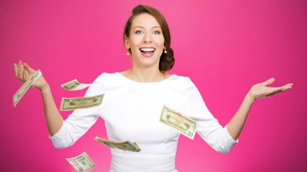 Mulher super animada, rindo, com notas de dólar voando no ar, em um fundo magenta isolado. Conceito de emoção positiva, de expressão facial e de sentimentos.