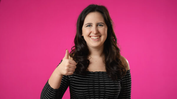 Retrato de uma mulher morena sorrindo, com um polegar para cima, posando, isolada em um estúdio de fundo rosa. Conceito de estilo de vida e de emoções sinceras de pessoas.