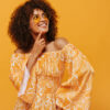 Mulher usando um óculos escuros, sorrindo, em um cenário isolado, pensativa, posando em em um fundo amarelo.