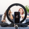 duas meninas sentadas no sofá em segundo plano com uma high light e uma celular mostrando o tik tok em primeiro plano