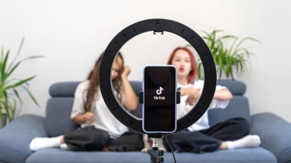 duas meninas sentadas no sofá em segundo plano com uma high light e uma celular mostrando o tik tok em primeiro plano