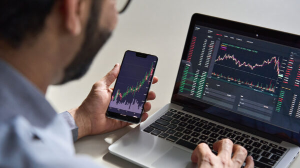 homem com um celular na mão e com notebook na frente acompanhando o mercado de investimento