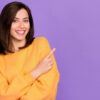 mulher sorridente com blusa laranja e em fundo roxo