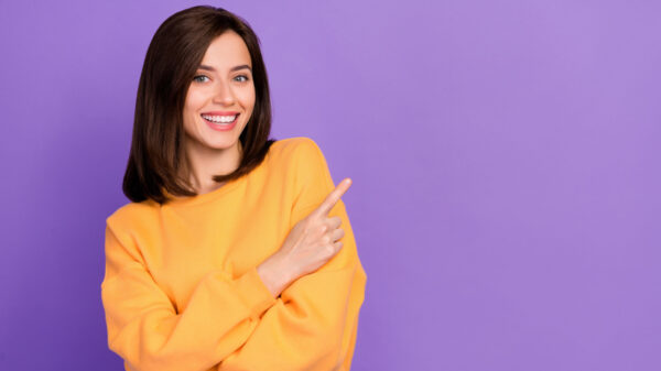 mulher sorridente com blusa laranja e em fundo roxo
