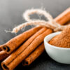 paus de canela e pote branco com canela em pó em cima de uma mesa cinza