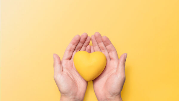 Mãos segurando um coração de resina amarela contra um fundo amarelo correspondente, simbolizando a conscientização sobre a saúde mental e o significado do Setembro Amarelo. Conceito de bem-estar mental e prevenção do suicídio.