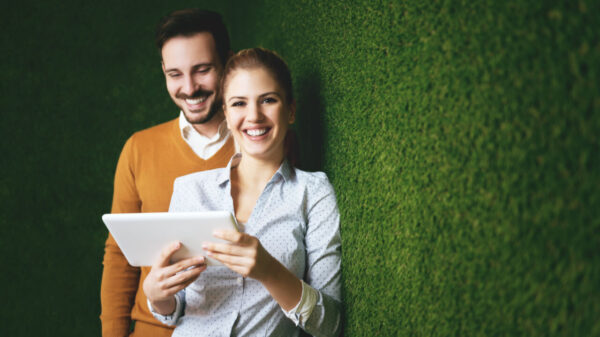Um homem e uma mulher segurando um tablet, em pé, sobre um muro de grama verde.