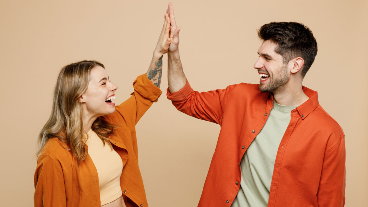 Casal feliz de amigos (homem e mulher) usando roupas casuais, juntos, reunidos, cumprimentando um ao outro, isolados em um fundo liso de cor bege clara.