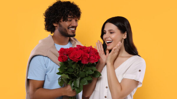 homem segurando um buque de rosas e entregando para uma mulher em fundo amarelo