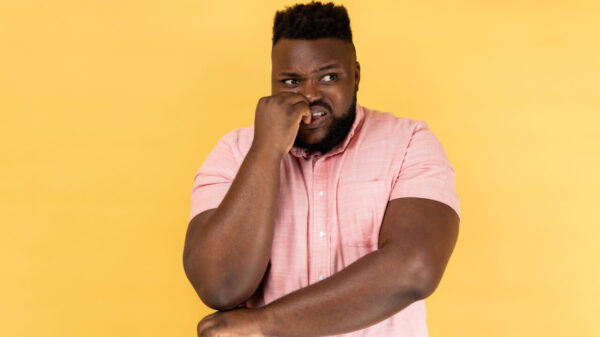 Retrato de um homem estressado e preocupado, usando uma camisa rosa, roendo as unhas, nervoso, com problemas, em pânico, parecendo assustado, desviando o olhar. Estúdio interno isolado em um fundo amarelo.