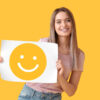 Mulher segurando um papel com um emoticon sorridente, em um fundo amarelo.