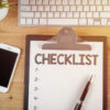 mesa de madeira com uma lista de checklist em papel sulfite e uma teclado branco acima