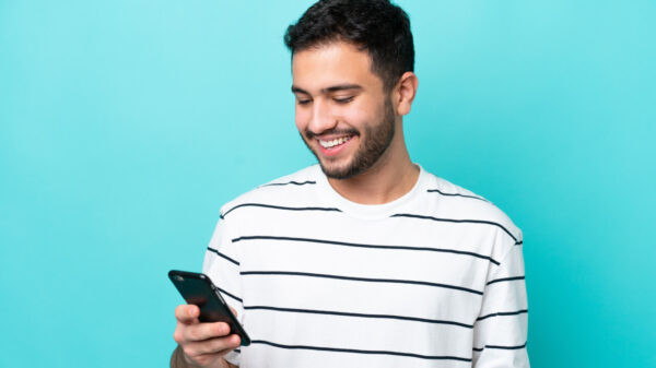 Homem isolado em um fundo azul usando um celular.