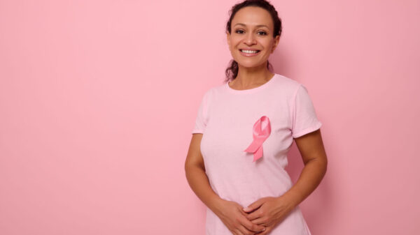 Mulher sorrindo, usando uma camiseta rosa com uma fita de cetim rosa simbolizando o Dia Internacional do Câncer de Mama, expressando solidariedade e apoio aos pacientes e sobreviventes de câncer de mama.