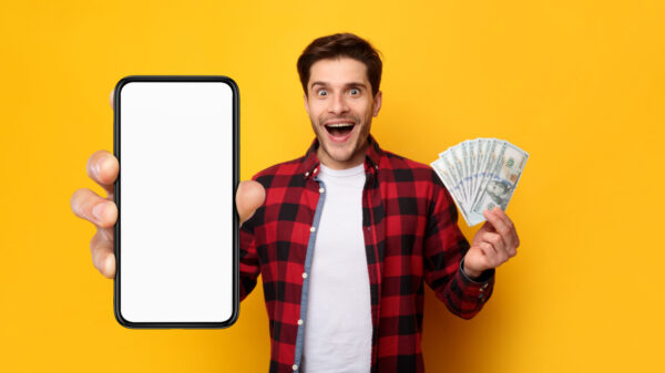 homem segurando um celular na mão esquerda e um leque de dinheiro na mão direita em fundo amarelo
