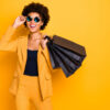 mulher negra usando roupas amarelas e carregando sacolas de compras na cor preta em fundo amarelo