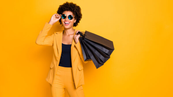 mulher negra usando roupas amarelas e carregando sacolas de compras na cor preta em fundo amarelo