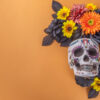 À direita há uma caveira mexicana com flores em fundo laranja