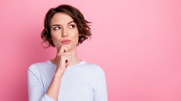 mulher branca vestindo roupa branca e com expressão facial pensativa em fundo rosa