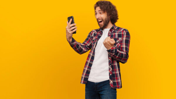 Homem, feliz, alegre, olhando para o celular em um fundo amarelo.