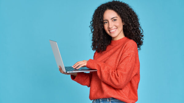 Mulher feliz usando um notebook, isolada em um fundo azul, sorrindo.