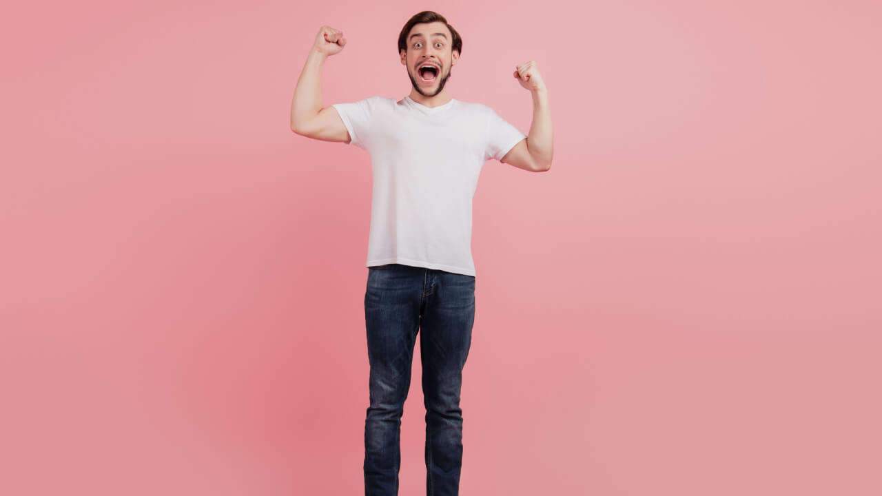 Foto em tamanho real de um homem alegre e sortudo comemorando, isolado sobre um fundo de cor rosa.