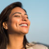 mulher de olhos fechados e sorrindo em um ambiente em céu aberto