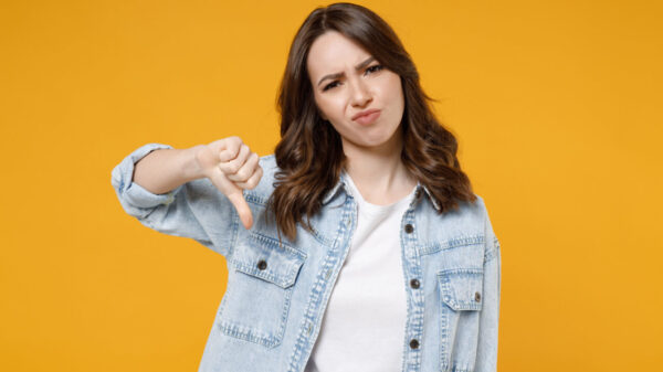 mulher branca fazendo um sinal de negativo com o dedo, ela usa jaqueta jeans e está em um fundo amarelo