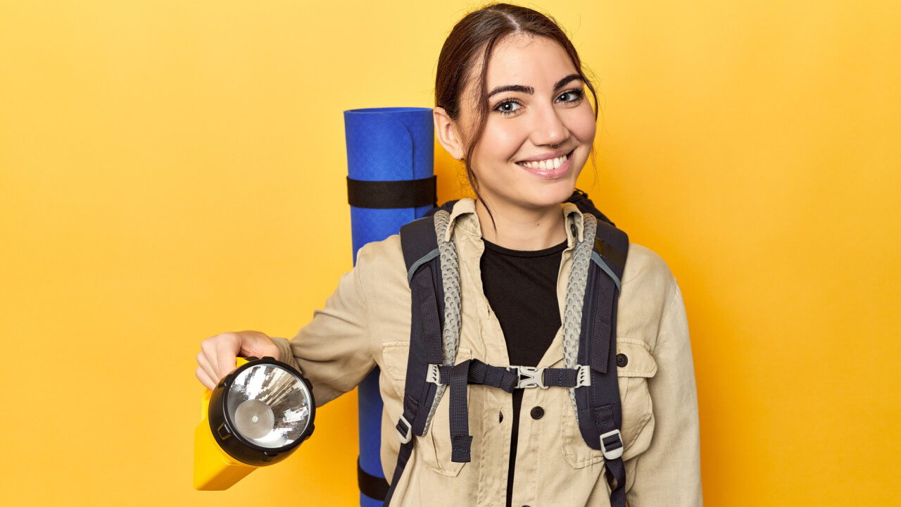 Mulher com uma mochila nas costas, segurando uma lanterna.