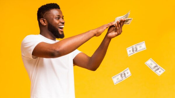 na esquerda está um homem negro vestido camisa branca com notas de dinheiro na mão e jogando pelo ar em fundo amarelo