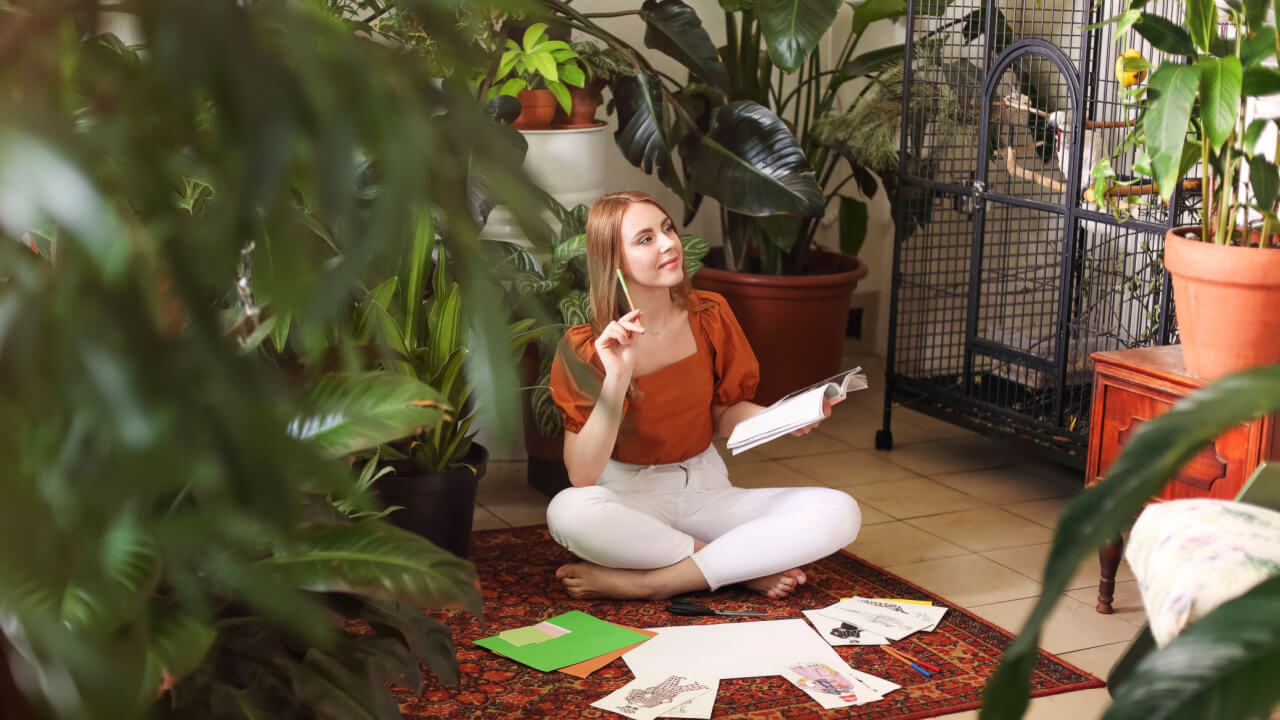 mulher sentada no chão segurando um livro em um ambiente cheio de plantas