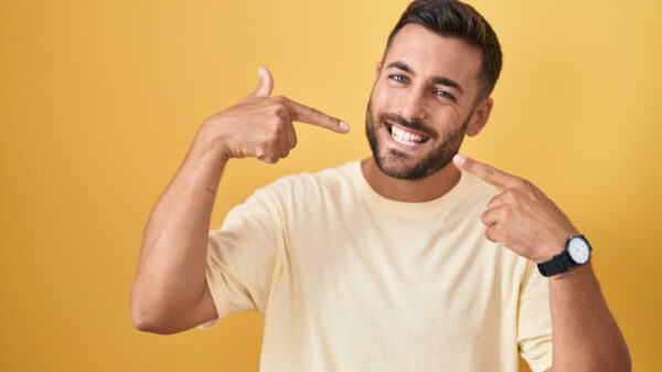 homem branco sorrindo com os dedos indicadores apontando o sorriso em fundo amarelo