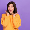 mulher branca de cabelo liso na altura dos ombros usando uma blusa laranja em fundo roxo