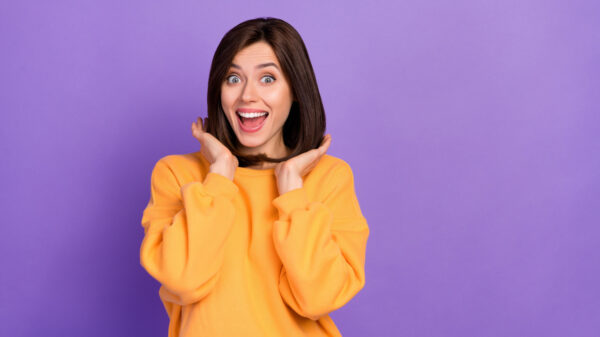mulher branca de cabelo liso na altura dos ombros usando uma blusa laranja em fundo roxo