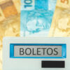 calculadora escrito boletos no visor e ao fundo notas de cinquenta com uma nota de cem reais ao meio