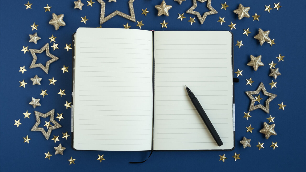 Um diário aberto, uma caneta e estrelas em um fundo azul. Conceito de planejar o ano-novo.