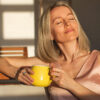 mulher de cabelo curto e loiro sentada em um sol recebendo sol solar e segurando uma caneca