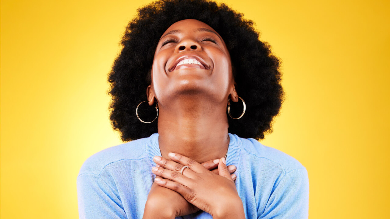 Mulher feliz, animada, em um fundo amarelo, com as mãos no peito, grata por sorte.