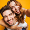 casal hétero com ela montada nas costas dele em fundo amarelo