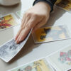 cartas de tarot em cima de uma mesa branca e com uma mão segurando uma dessas cartas