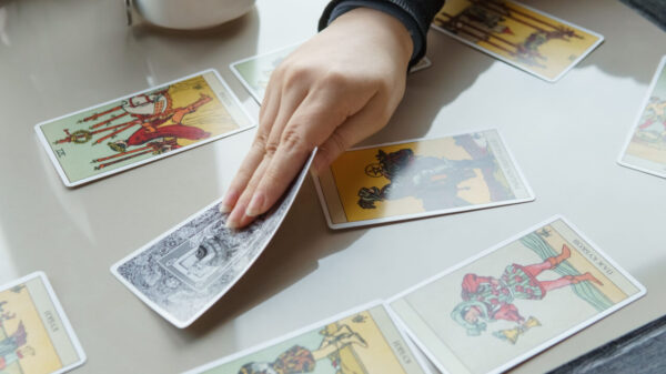 cartas de tarot em cima de uma mesa branca e com uma mão segurando uma dessas cartas