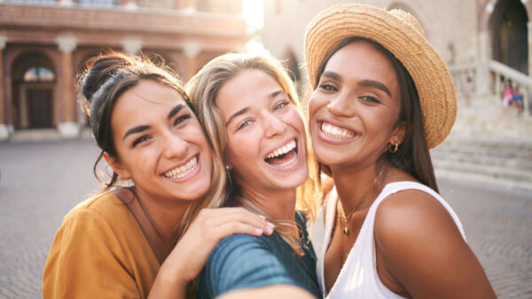 três amigas sorrindo tirando foto a céu aberto