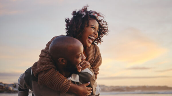 casal feliz na praia com ela montada nas costas dele