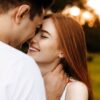 casal hetero sorrindo um para o outro com as testas próximas em um campo aberto