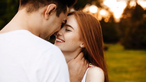 casal hetero sorrindo um para o outro com as testas próximas em um campo aberto