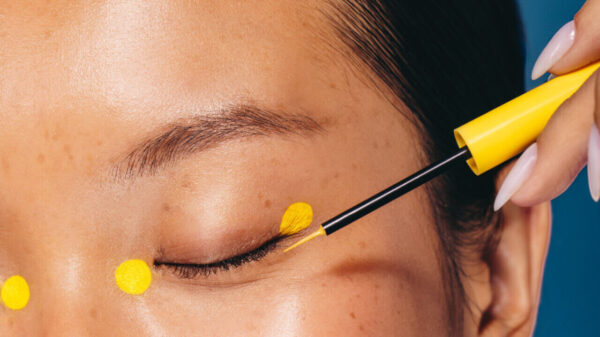 Mulher fazendo maquiagem com um produto cosmético, aplicando quatro pontos ao redor dos olhos usando um delineador amarelo, uma técnica de maquiagem.
