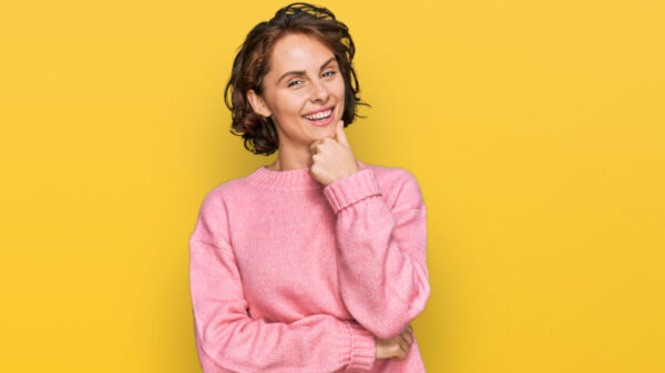 Mulher usando roupas casuais, parecendo confiante, olhando para a câmera, sorrindo, com os braços cruzados e uma mão no queixo, pensando positivo.