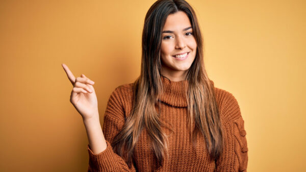 mulher sorrindo com um braço levantado e usando roupa marrom escuro em fundo marrom alaranjado