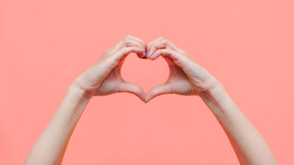 Mãos femininas fazendo um formato de coração, isoladas em um fundo salmão. Conceito de amor, harmonia, gratidão, sentimentos e emoções.
